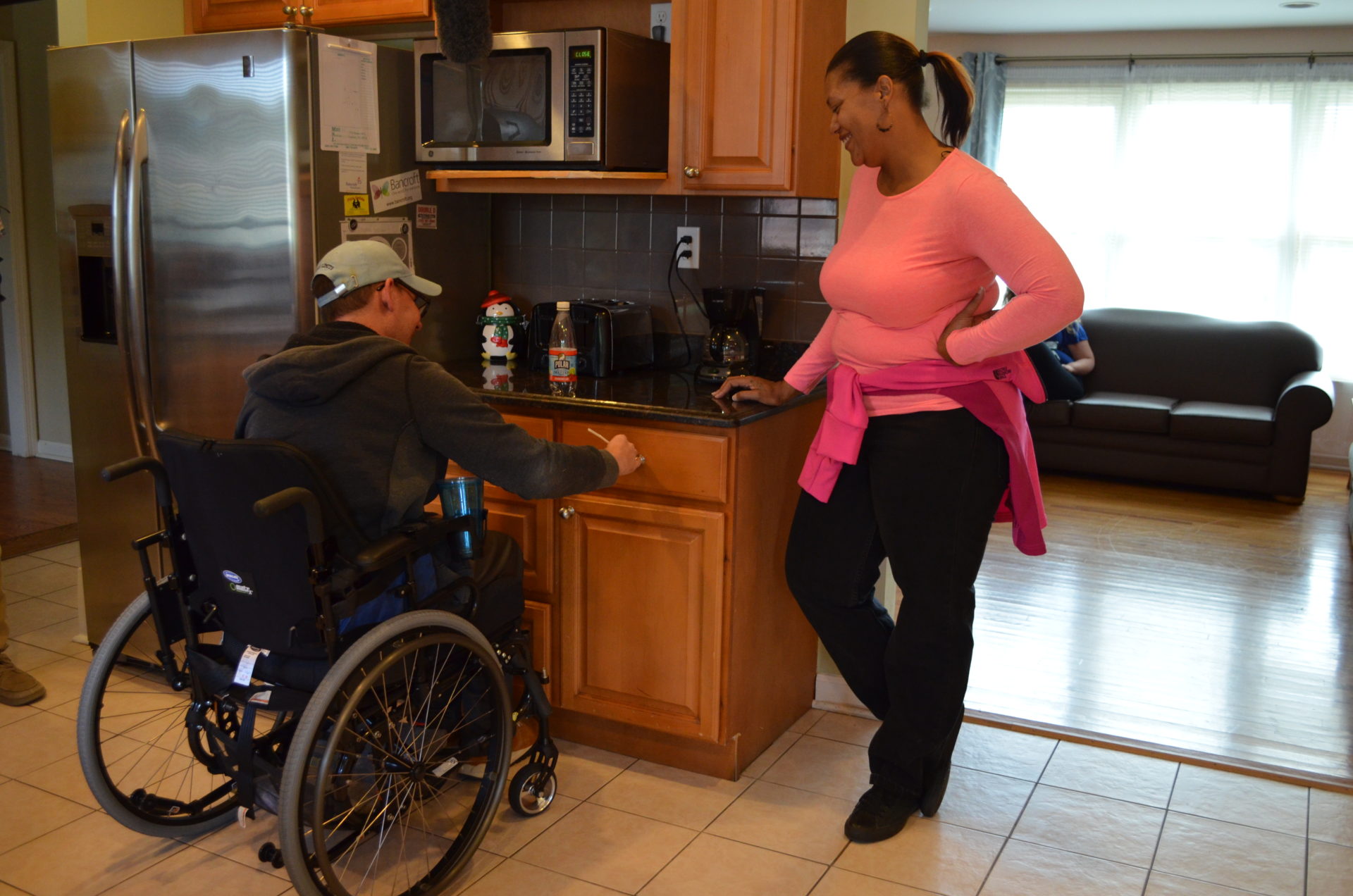 Bancroft NeuroRehab patient sitting in wheelchair on the left with a clinician to his right. They are both by a countertop in the kitchen.