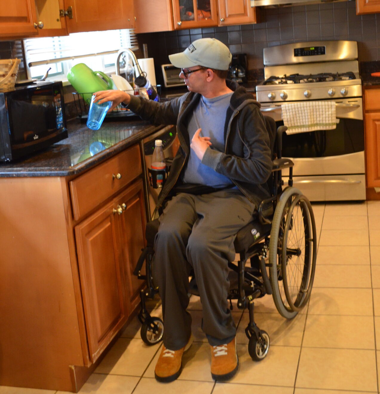 Bancroft NeuroRehab patient in a wheelchair is in his kitchen holding a blue cup.