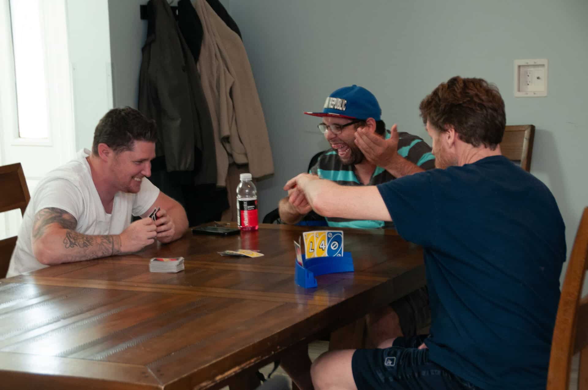 3 men seated at a dining room table playing uno and laughing together