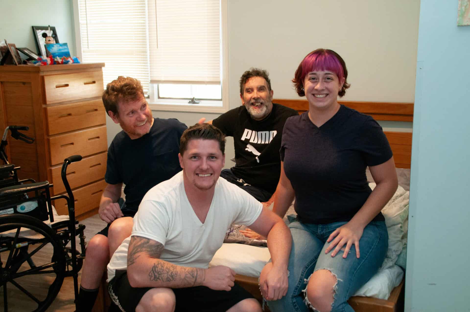 4 individuals seated in a bedroom, smiling at the camera.