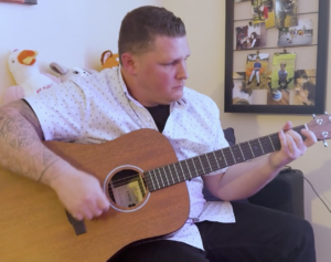 A man in a white shirt and tattoos plays guitar