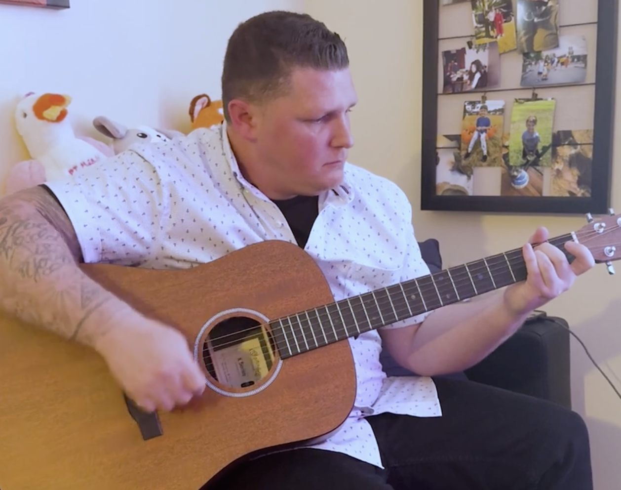 A man in a white shirt and tattoos plays guitar